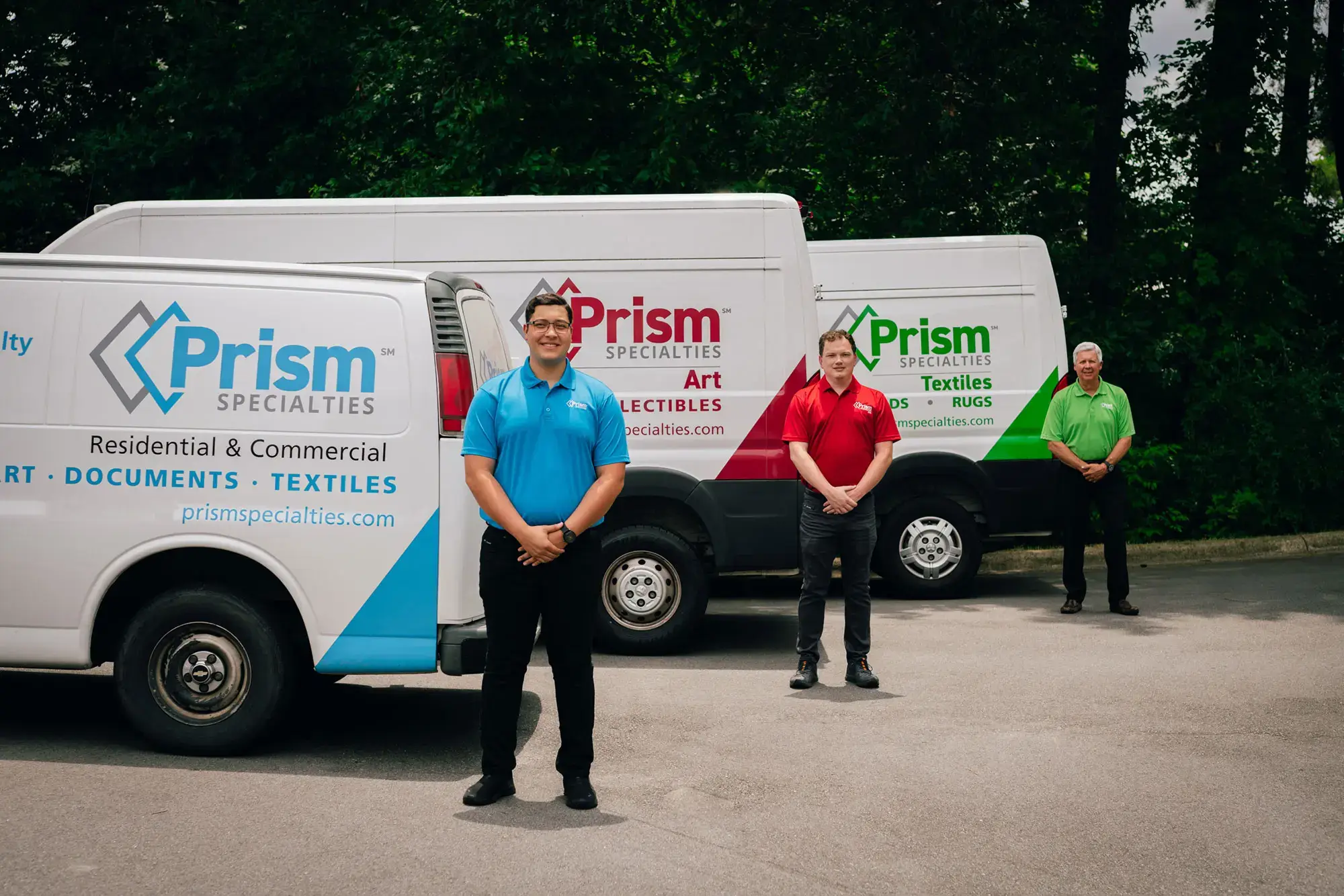 Prism Specialties team members in blue, red, and green t-shirts standing next to corresponding Prism Specialties vans.